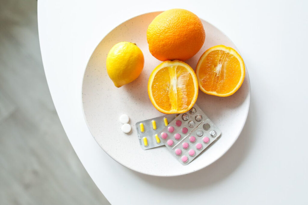 A plate of fresh citrus fruits and blister packs of pills for immune health