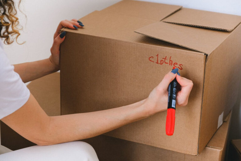 A woman labeling a cardboard box with a red marker while decluttering
