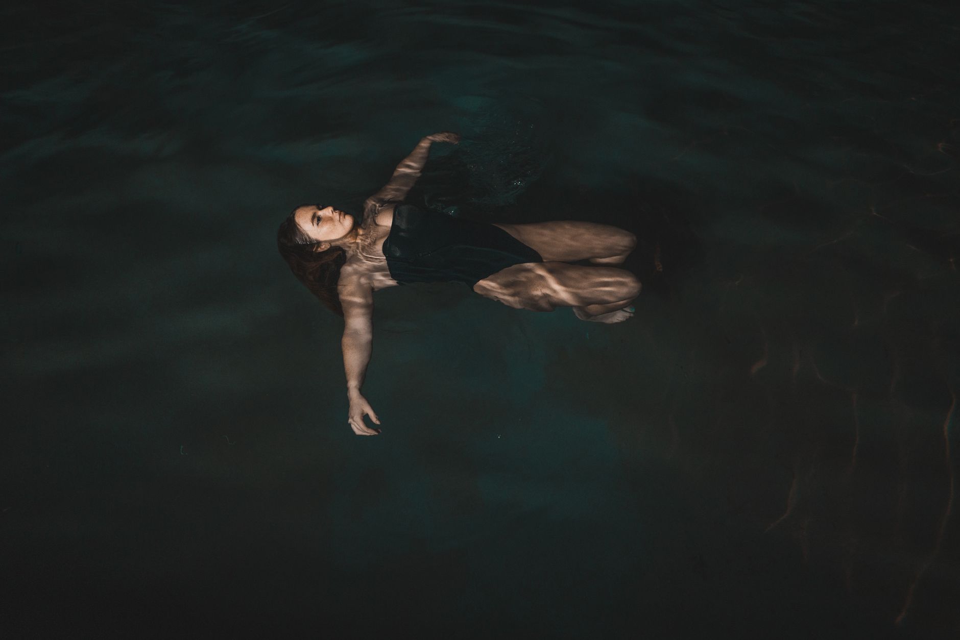 A person floating alone on their back in dark still water, seen from above at night.