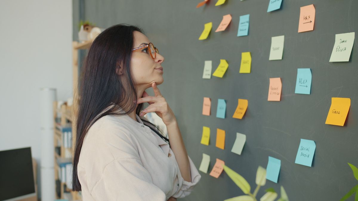 Thoughtful woman planning ideas on a chalkboard wall with colorful sticky notes in an office setting.