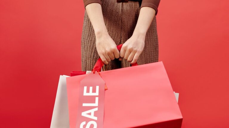 Close-up of a person holding shopping bags with a sale tag on a red background.