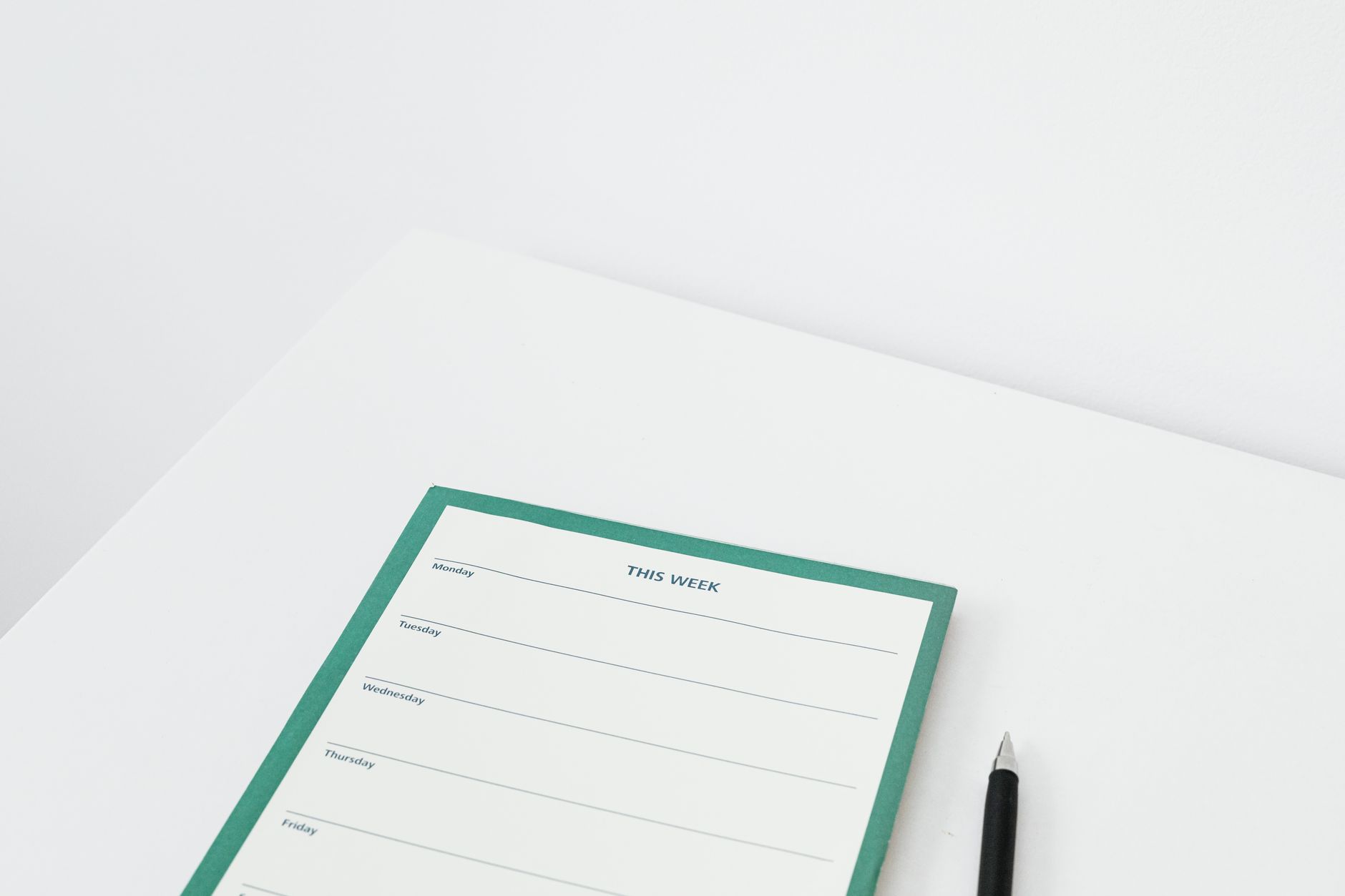 Minimalist weekly planner with a pen on a clean white desk, ready for scheduling the week ahead.
