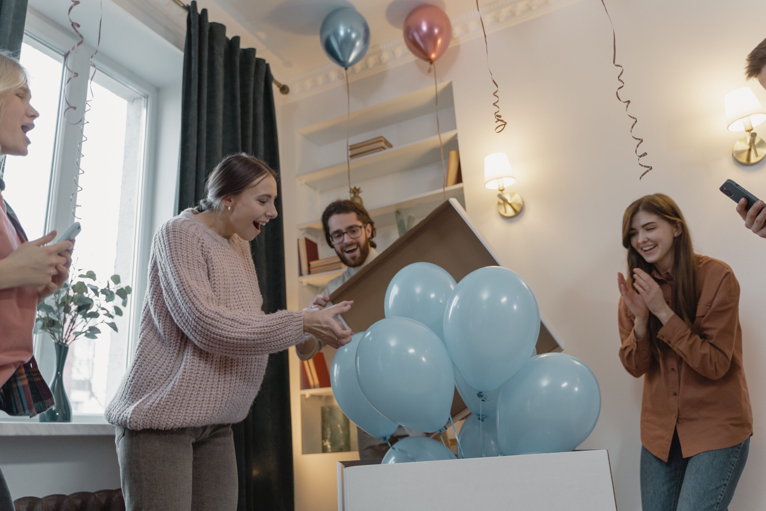Friends celebrating a gender reveal together with blue balloons indoors.