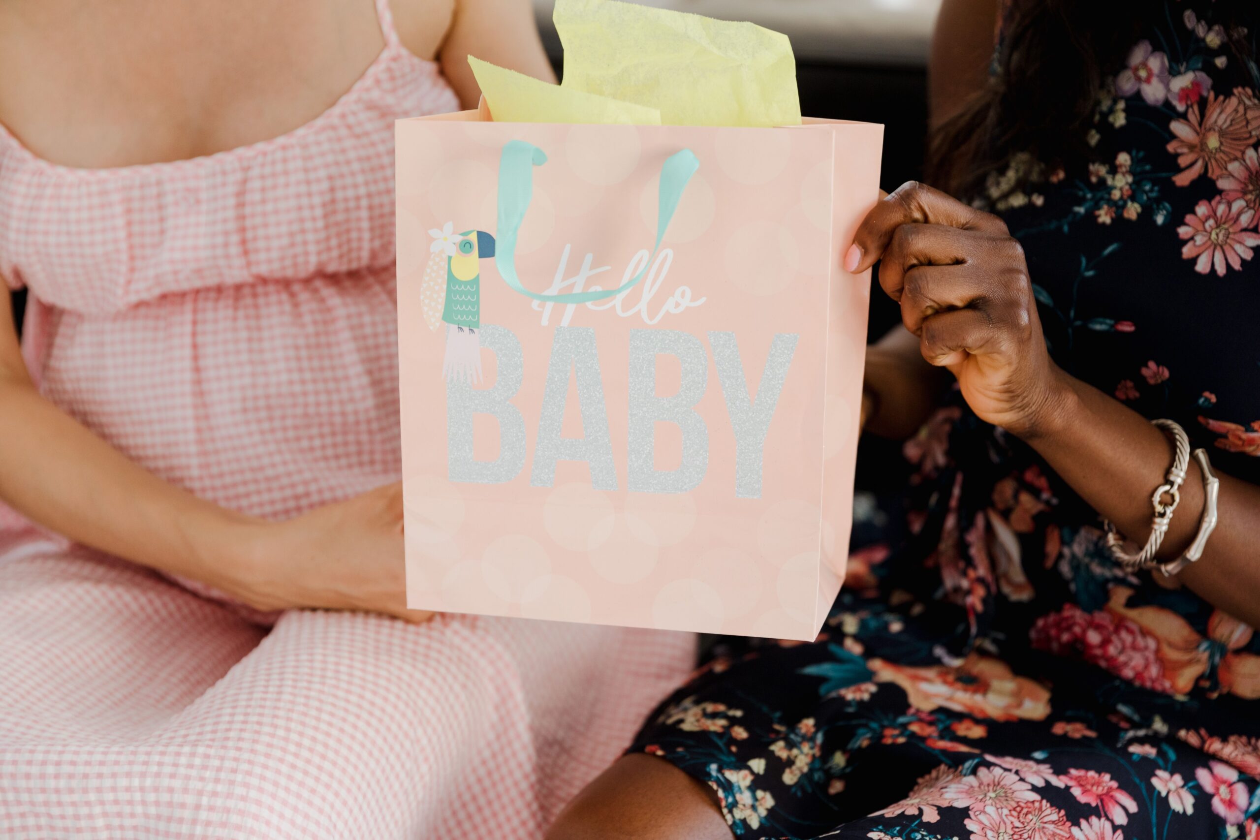 A close-up of an expectant mother sitting beside a wrapped gift bag at a celebration.