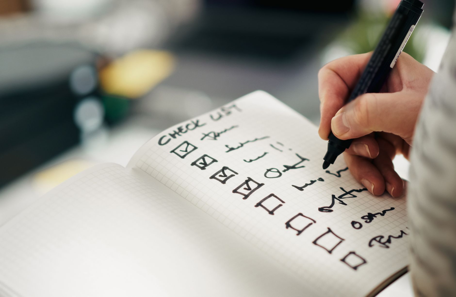 A hand ticking checked boxes on a printed checklist in a grid-paper notebook.